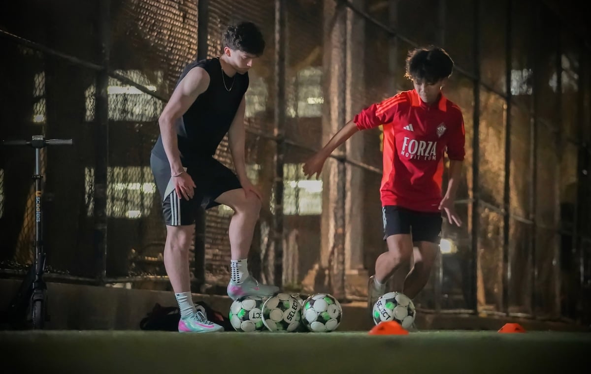 Adult soccer coach training young child with soccer balls on an indoor court with brick walls